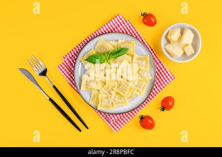 Leckeres, appetitliches Ravioli mit Käse und Basilikum auf einem Teller, hellgelber Hintergrund Stockfoto