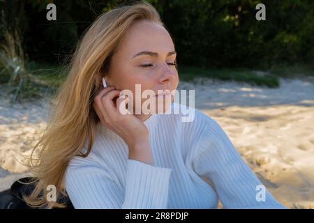 Glückliche junge Frau am Strand Meer Meer. Tragen von kabellosen Kopfhörern, die eine Audio-Heilklang-Therapie durchführen, während Sie sich der Natur bewusst sind. Wohlbefinden Einheit mit Natur Gesundheit Achtsamkeit. Genießen Sie Entspannung im Freien Stockfoto