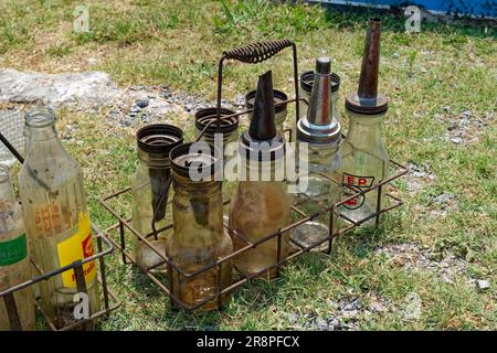 Eine Sammlung von verschiedenen gebrauchten Flaschen aus antikem Erdölglas in einem rostigen Metalldrahtträger, der auf dem Boden im Freien sitzt, Nahaufnahme Stockfoto