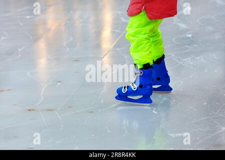 Ein Kind in hellgrünen Hosen, einer roten Jacke und blauen Stiefeln lernt, unsichere Schritte zu machen. Nahaufnahme, Kopierbereich. Stockfoto