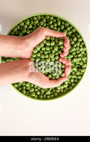 Nahaufnahme von vielen reifen Erbsen in den Händen, herzförmig. Grüne Erbse in einer grünen Schüssel. Leckere und gesunde Speisen. Gemüse Stockfoto