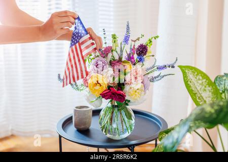 Unabhängigkeitstag der USA. Die Frau legt die amerikanische Flagge in eine Vase mit Blumen, die ihr Zuhause schmücken. Juli 4. Gedenktag Stockfoto