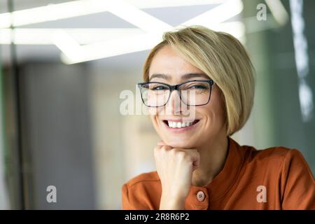 Nahaufnahme einer schönen blonden Geschäftsfrau im Büro, einer Brillenarbeiterin, die lächelt und in die Kamera schaut, Porträt einer glücklichen Frau Stockfoto