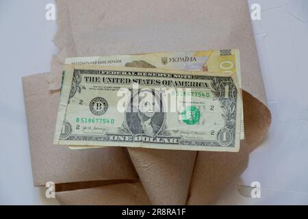 Ein amerikanischer Dollar und einhundert ukrainische Hrywna liegen auf Toilettenpapier auf einer Nahaufnahme mit weißem Hintergrund Stockfoto