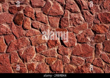 Eine alte Mauer aus rohem, rotem, angebautem Naturstein Stockfoto