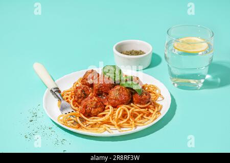 Teller mit gekochter Pasta mit Tomatensoße und Fleischbällchen auf blauem Hintergrund Stockfoto