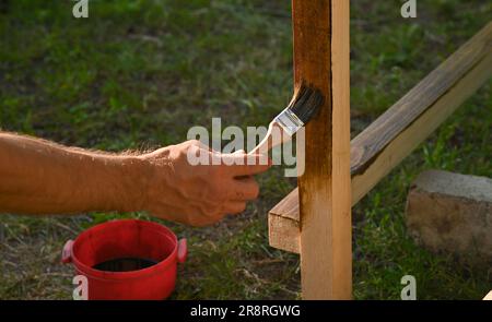 Ein Mann kann eine Schutzschicht auf Holzbalken mit einem Pinsel auftragen. Im Freien Stockfoto