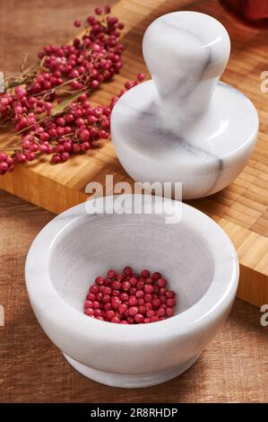 Trockener Rosenpfeffer in weißem Marmormörtel neben dem Stößel Stockfoto