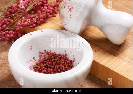 Trockener Rosenpfeffer in weißem Marmormörtel neben dem Stößel Stockfoto