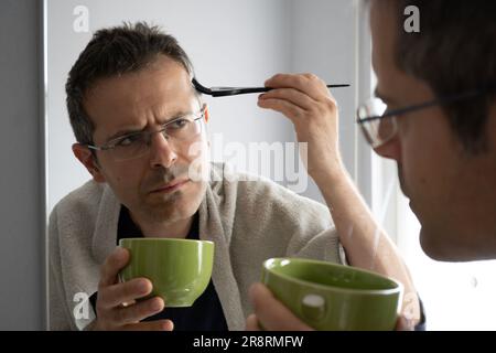 Ein Mann mittleren Alters mit weißem Haar färbt sich die Haare im Spiegel Stockfoto