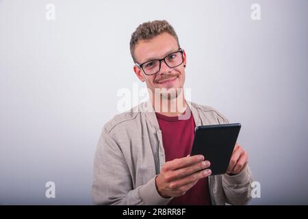 Ein lächelnder junger Mann benutzt sein Tablet, Studioaufnahme mit weißem Hintergrund Stockfoto