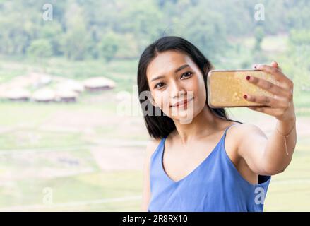 Eine junge Frau mit Smartphone macht ein Selfie-Foto in einer tropischen Landschaft Stockfoto