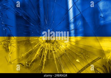 Einschussloch, Risse im Glas auf gelb-blauem Hintergrund. Ukrainische Flagge auf gebrochenem Glas. Konzept: Russisch-ukrainischer Krieg. Stockfoto