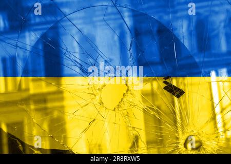 Einschussloch, Risse im Glas auf gelb-blauem Hintergrund. Ukrainische Flagge auf gebrochenem Glas. Konzept: Russisch-ukrainischer Krieg. Stockfoto
