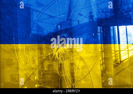 Einschussloch, Risse im Glas auf gelb-blauem Hintergrund. Ukrainische Flagge auf gebrochenem Glas. Konzept: Russisch-ukrainischer Krieg. Stockfoto