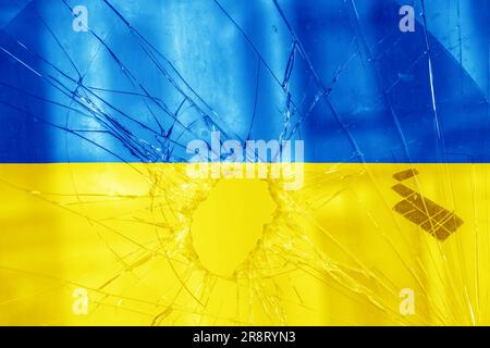 Einschussloch, Risse im Glas auf gelb-blauem Hintergrund. Ukrainische Flagge auf gebrochenem Glas. Konzept: Russisch-ukrainischer Krieg. Stockfoto