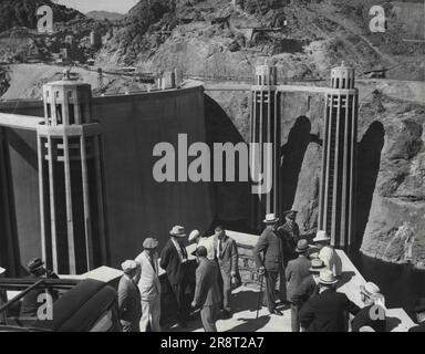 Präsident Roosevelt sieht das riesige Boulder-Dam-Projekt – Präsident Roosevelt (trägt Hut und trägt Cane) wird mit Mitgliedern seiner Partei gezeigt, die über das riesige Felsdamm-Projekt blicken, bevor er heute hier seine engagierte Rede hält. Die Präsidentschaftsfeier sieht das gigantische Projekt, das jetzt mit Ausnahme der Kraftwerke abgeschlossen ist, von der Arizona-Seite des Colorado River mit der Nevada-Seite im Hintergrund. Der Damm stellt die erstaunlichste technische Leistung des Menschen dar. Seine Betonmauern erheben sich 727 Fuß über dem Flussbett. Einer der beiden Ansaugtürme auf t… Stockfoto
