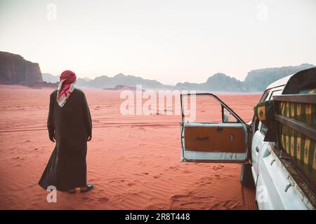 Beduinen-Fahrer-Tour-Organisator steht in der Wadi-Rum-Wüste mit einem Allradfahrzeug nach Sonnenuntergang. Besuchen Sie Jordanien Touren im berühmten Wadi Rum Reserve Mitte Stockfoto