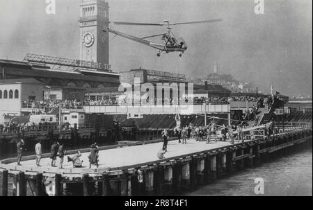 Der Hubschrauberhafen öffnet sich – der erste öffentliche Hubschrauberlandebereich des Westens wurde heute offiziell eröffnet, im Schatten des historischen Ferry Building (Turmhintergrund). Der erste Helikopter, der landen soll, steht am Dock, während ein zweiter darüber schwebt, während er eine Person (im Stuhl des Bootswains) von einem kleinen Schiff in der Bucht überführt. 28. Februar 1950. (Foto von AP Wirephoto). Stockfoto