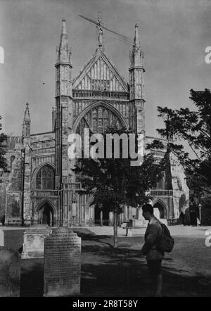 Grabstein mit Moral -- Ein Blick auf die Winchester Kathedrale, mit dem amüsanten Grabstein im Vordergrund. Ein amüsanter Grabstein ist vor der Winchester Cathedral, Winchester, Hampshire zu sehen. Es ist dem Gedenken an einen Grenadier der Hampshire-Miliz gewidmet, der nach der Inschrift „durch das Trinken von kleinem Bier, wenn heiß“ am 12. Mai 1764 im Alter von 26 Jahren starb. Es scheint, als sei es gefährlich, kaltes kleines Bier zu trinken, wenn man es nicht ist, daher die Warnung an andere, die auf seinem Grabstein enthalten ist. 13. Mai 1946. (Foto von der Fachpresse). Stockfoto