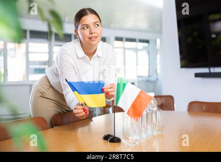 Vorbereitung auf Geschäftsverhandlungen - Frau setzt kleine Flaggen von Ländern der Ukraine und Italiens auf den Tisch Stockfoto