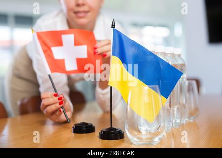 Ein nicht wiedererkennbares Mädchen setzt Zwergflaggen der Ukraine und der Schweiz vor internationalen Verhandlungen Stockfoto