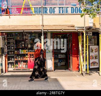 Eine Frau in muslimischem Kleid, die die North End Road entlang geht, Fulham, London, vorbei an einem Führerschein namens Hair of the Dog Stockfoto