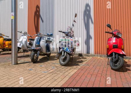 Eine Reihe von Motorrollern, die in einer Straße geparkt sind. Moderner Roller. Vespa und Lambretta haben geparkt. 1960er Popkultur. Stockfoto