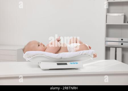 Niedliches kleines Baby, das in der Klinik auf einer Waage liegt Stockfoto