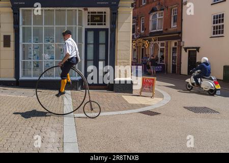 Ein Kontrast von Alt und Neu, wie ein Penny-Far-Fahrrad und ein Motorroller an einer Kreuzung verschiedene Routen nehmen. Eine Person, die einen Penny fährt. Stockfoto