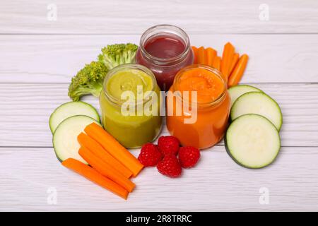 Gläser mit gesunder Babynahrung und Zutaten auf weißem Holztisch Stockfoto