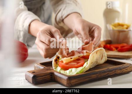 Eine Frau, die köstliche Pita-Wrap mit Jamon, Käse und Gemüse am Holztisch kocht, Nahaufnahme Stockfoto