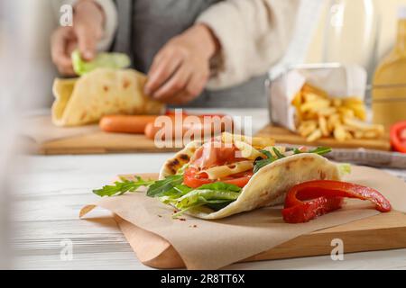 Frau, die köstliche Pita Wrap mit Jamon, Käse und Gemüse am Holztisch kocht. Konzentriere dich auf die Schale Stockfoto