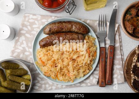 Teller mit Sauerkraut und Würstchen, serviert auf einem hellgrauen Tisch, flach liegend Stockfoto