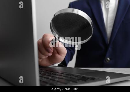 Ein Mann, der die Lupe neben dem Laptop am Tisch hält, Nahaufnahme. Konzept der Online-Suche Stockfoto