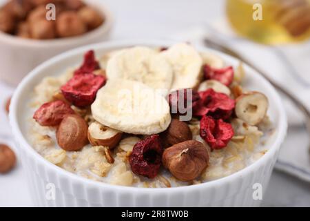 Köstlicher Haferbrei mit gefriergetrockneten Beeren, Bananen und Haselnüssen auf dem Tisch, Nahaufnahme Stockfoto