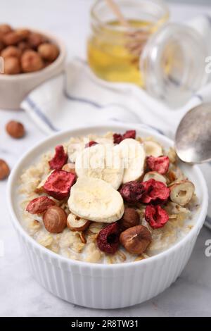 Köstlicher Haferbrei mit gefriergetrockneten Beeren, Bananen und Haselnüssen auf weißem Tisch, Nahaufnahme Stockfoto