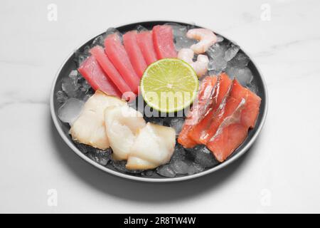 Sashimi-Set (rohe Scheiben von Thunfisch, Lachs, öligem Fisch und Garnelen) serviert mit Limette und Eis auf einem weißen Marmortisch Stockfoto