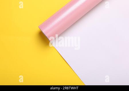 Rolle rosafarbenes Geschenkpapier auf gelbem Hintergrund, Draufsicht. Platz für Text Stockfoto