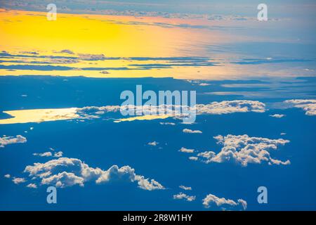 Blick auf die Wolken vom Flugzeugfenster bei Sonnenuntergang über den Wolken. Wolken und Sonne am Himmel. Die Sonne strahlt ein helles gelbes Licht aus, das den beleuchtet Stockfoto