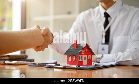 Nahaufnahme eines professionellen männlichen Immobilienmaklers oder maklers, der einer Kundin an einem Tisch im Büro die Hand schüttelt. Immobilieninvestition und Stockfoto