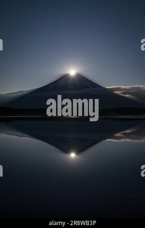 Der Vollmond, der über dem Gipfel des Mt. Fuji und das kopfüber liegende Bild des Mt. Fuji Stockfoto