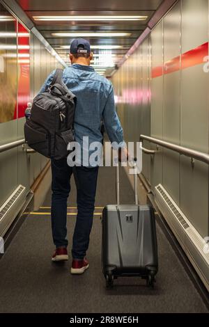 Ein Mann Mit Rucksack, Koffer Im Flughafenterminal, Rückansicht Von Mann Auf Dem Weg Zum Flugsteig. Geschäftsreisen, Urlaub Stockfoto