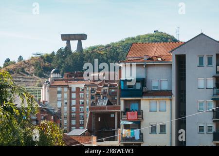 Das große Betondenkmal für gefallene Bergleute spomenik steht hoch auf einem Hügel hinter Wohngebäuden in Mitrovica, Kosovo Stockfoto