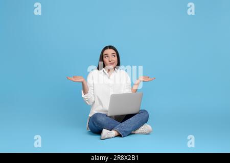 Verwirrte junge Frau mit einem Notebook auf hellblauem Hintergrund Stockfoto