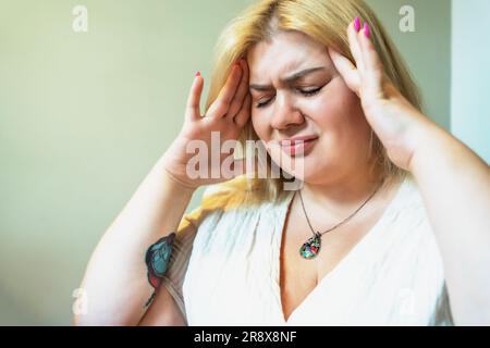 Übergewichtige, große blonde Frau, die den Kopf mit der Hand berührt, Schmerzen oder Kopfschmerzen oder Stress Depressionen Probleme mit psychischer Gesundheit. Stockfoto