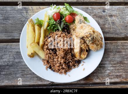 Hähnchen in Teig mit Reis, Bohnen, Mehl, Pommes frites und gemischtem Salat auf einem Holztisch. Typisch venezolanisches Gericht Stockfoto