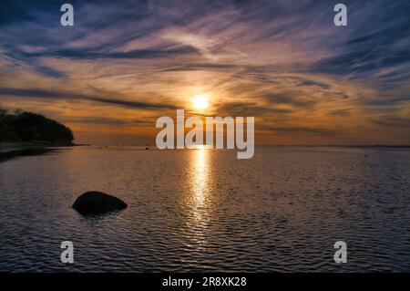 Sonnenuntergang, kleine Felsen im Wasser am Ufer. Lichtwellen. Poelinsel an der Ostsee. Naturfoto von der Küste Stockfoto