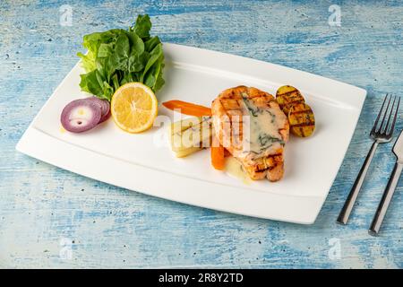 Gegrillter Lachs in Sauce mit Gemüse und Kartoffeln auf einem weißen Porzellanteller Stockfoto