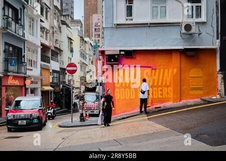 Hongkong, China - April 24 2023: Ein Mann malt die Wand orangefarben an, um Burger-Schilder in der Mitte abzudecken Stockfoto